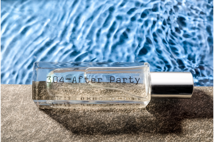 Perfume bottle labeled '304 After Party' on sand with water background