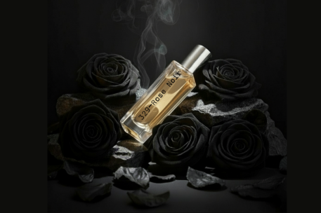 Perfume bottle with gold cap on black roses against a dark background