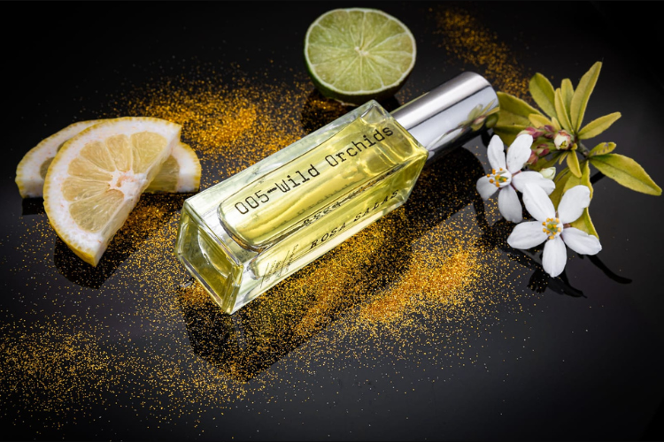 Perfume bottle labeled '005 Wild Orchid' with lemon slices, lime, and flowers on a dark background