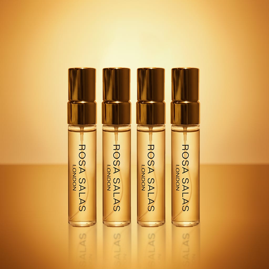 Four Rosa Salas London perfume bottles on a reflective surface with a warm gradient background.
