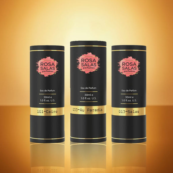 Three black cylindrical Rosa Salas perfume bottles on a reflective orange surface with a warm glow